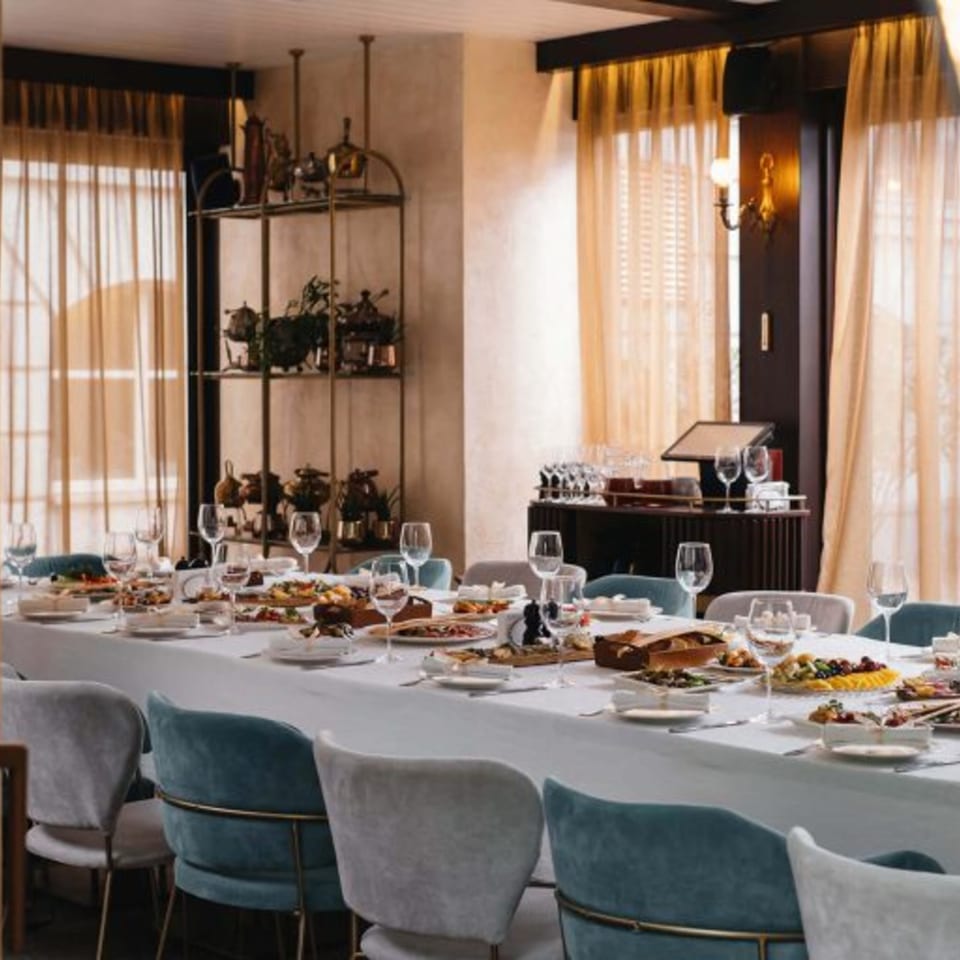 A long dining table set with food, glasses, and blue and grey chairs in a restaurant.