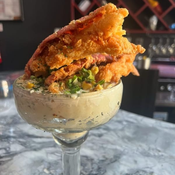 A margarita glass filled with creamy dip, topped with crispy fried chicken and green onions.