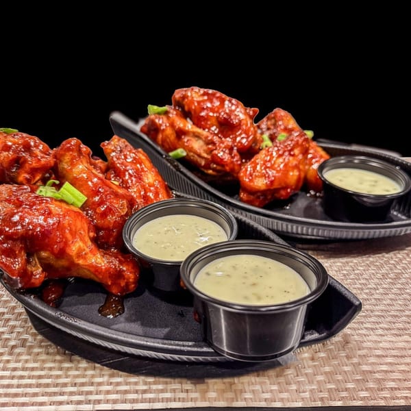 Two plates of TNT Rooftop Restaurant's spicy chicken wings with green onions and dipping sauce.