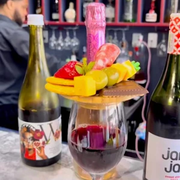 A wine glass with red wine, topped with a charcuterie board and a pink champagne bottle.