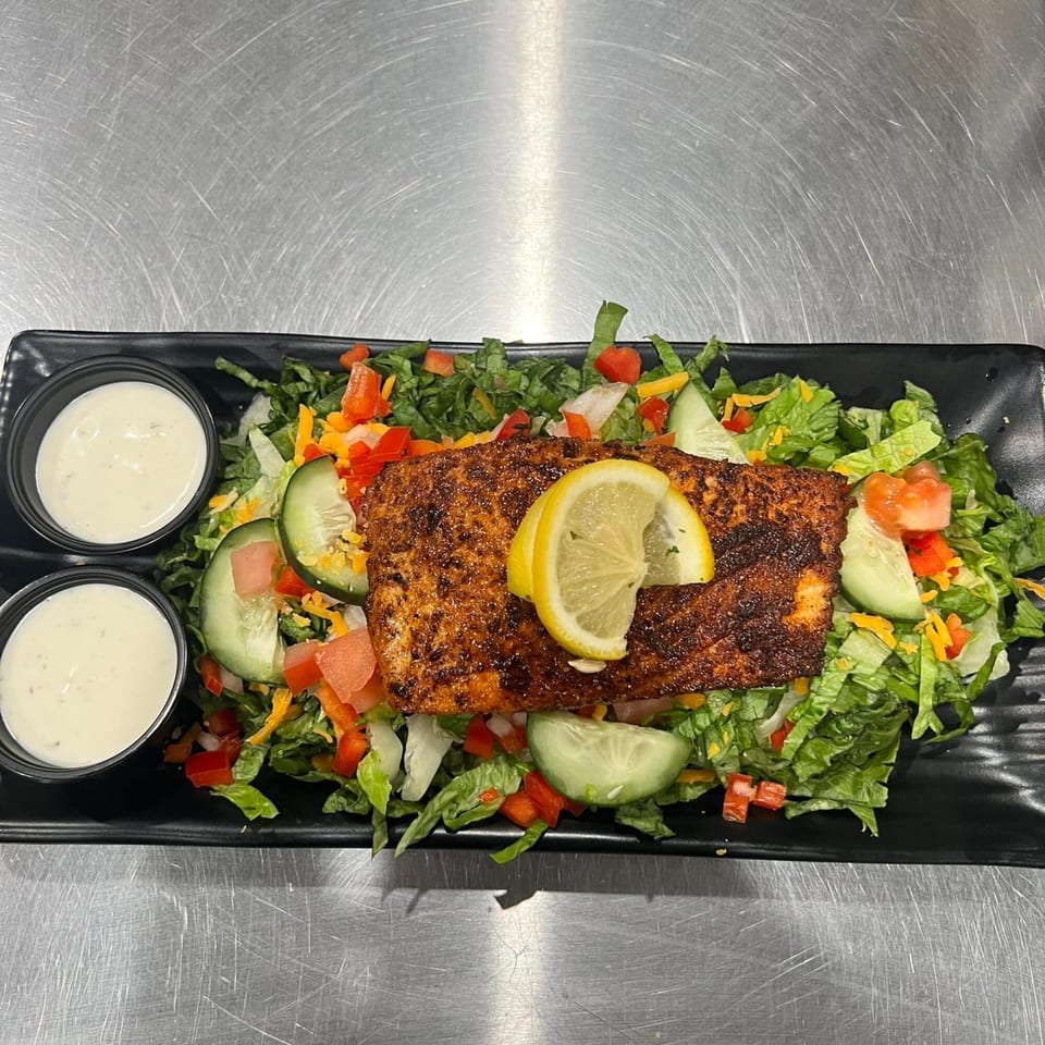 Blackened salmon salad with lettuce, tomatoes, cucumbers, cheese, and two cups of dressing.