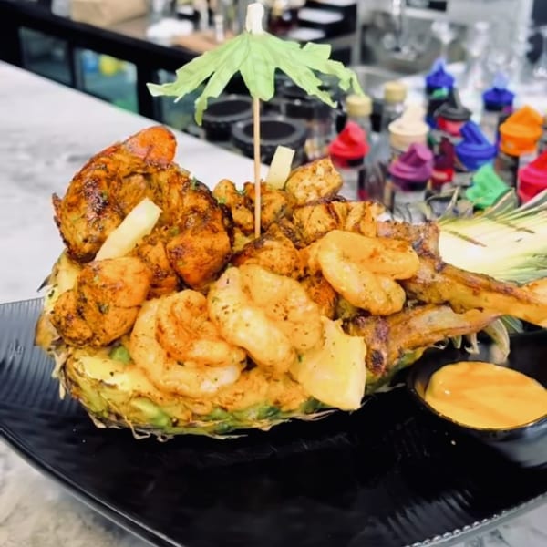 Grilled shrimp and chicken served in a pineapple half with a side of sauce.