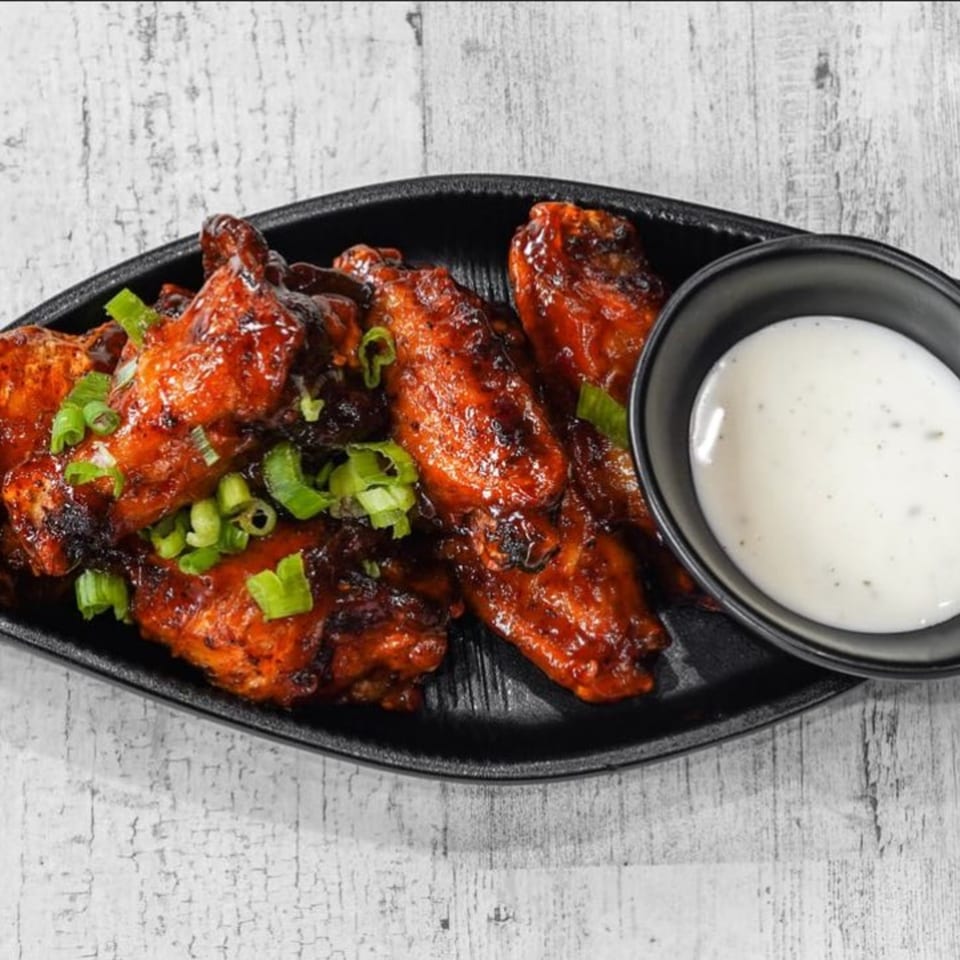 TNT Rooftop Restaurant's BBQ chicken wings, garnished with green onions, served with a side of ranch.