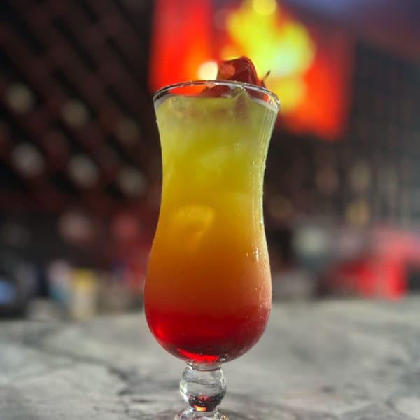 A vibrant, layered cocktail with red, orange, and yellow hues, garnished with fruit, on a bar.