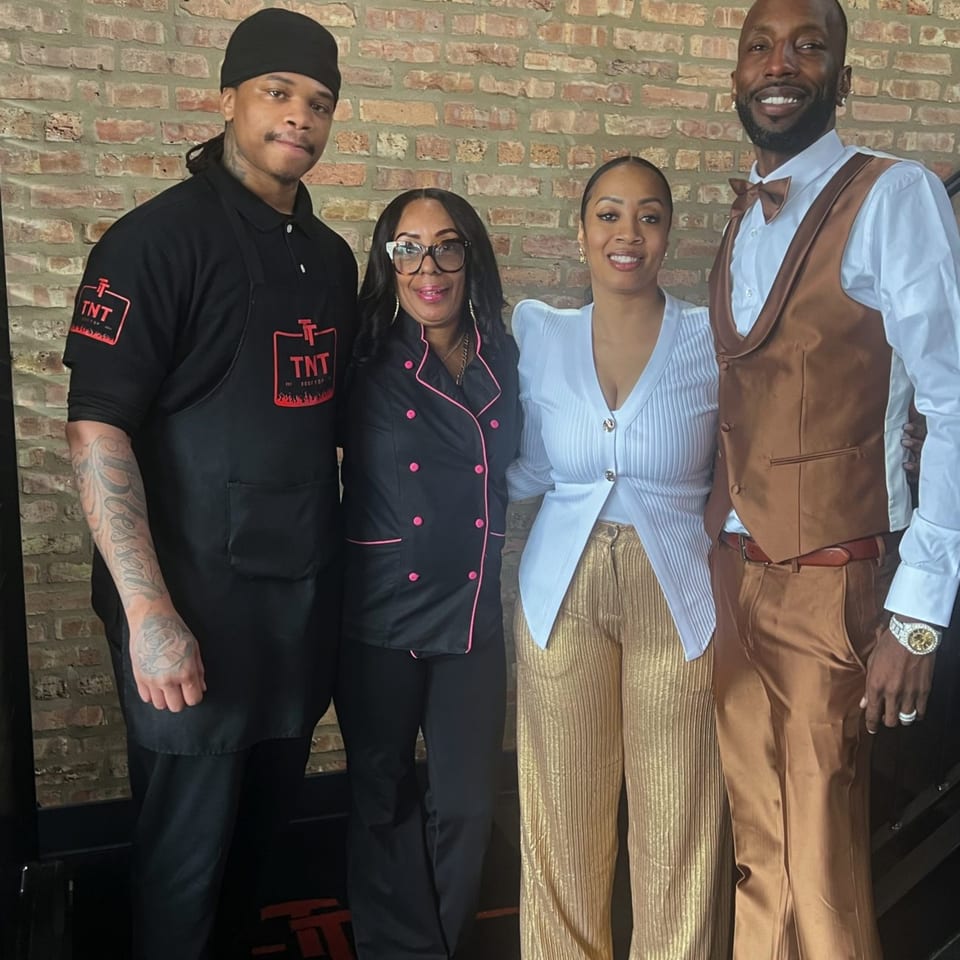 Four TNT Rooftop Restaurant staff members, two men and two women, stand smiling against a brick wall.