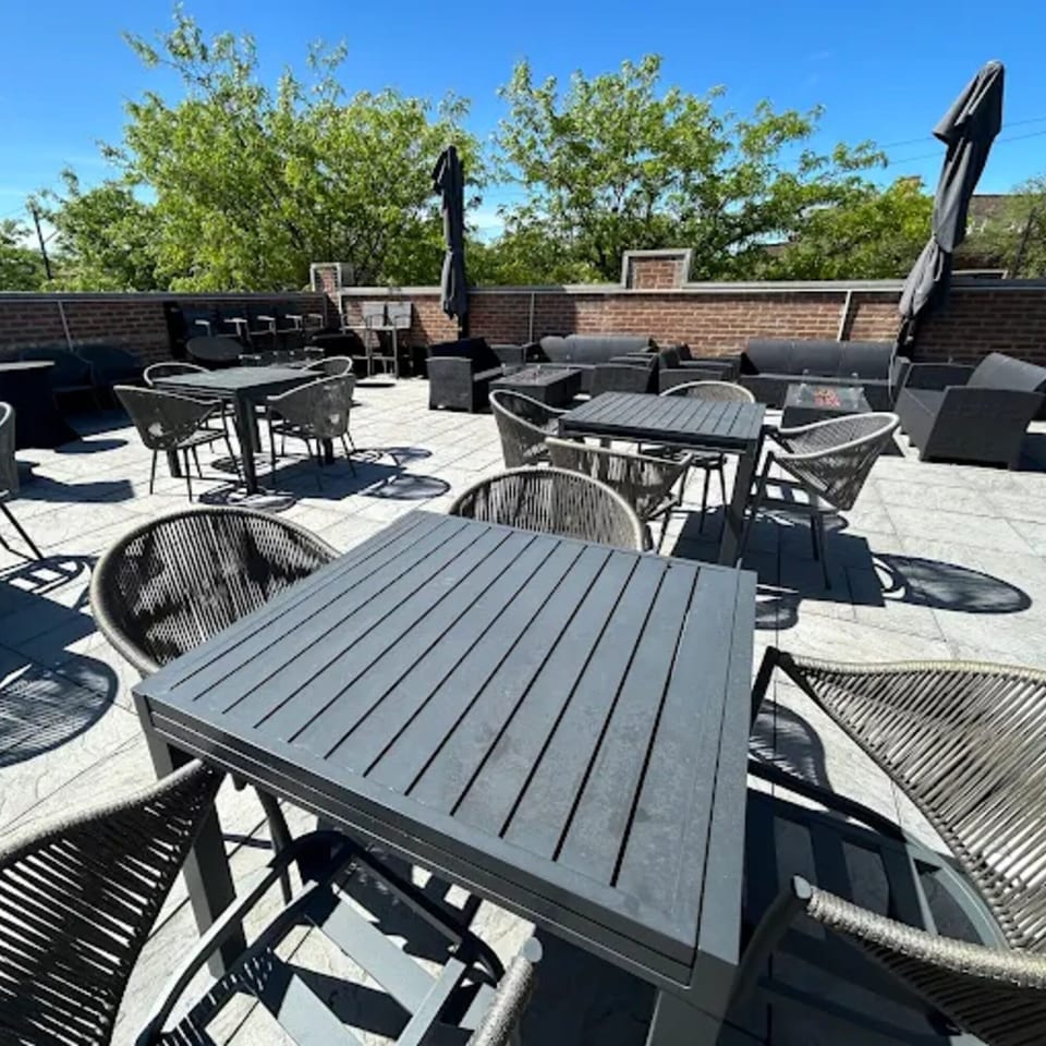 TNT Rooftop Restaurant's outdoor patio with dark tables, chairs, and lounge seating under a blue sky.