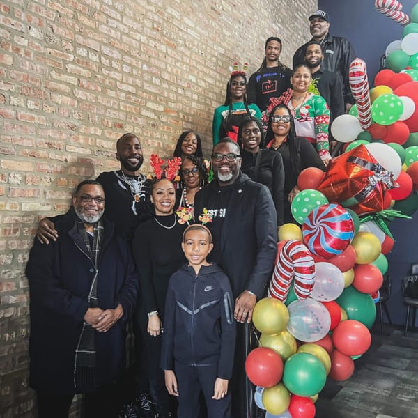 A large group of people, including children, pose on stairs next to a festive balloon arch.