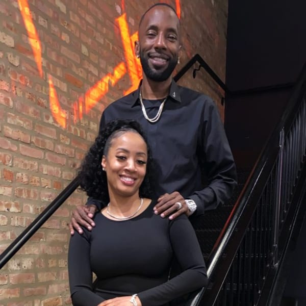 Smiling couple in black outfits posing on a staircase with a brick wall background at TNT Rooftop Restaurant.